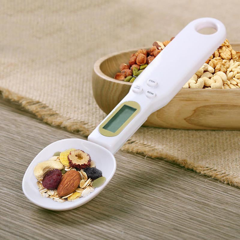 Digital kitchen scale measuring pasta with a hand holding it, on a green and white striped surface.